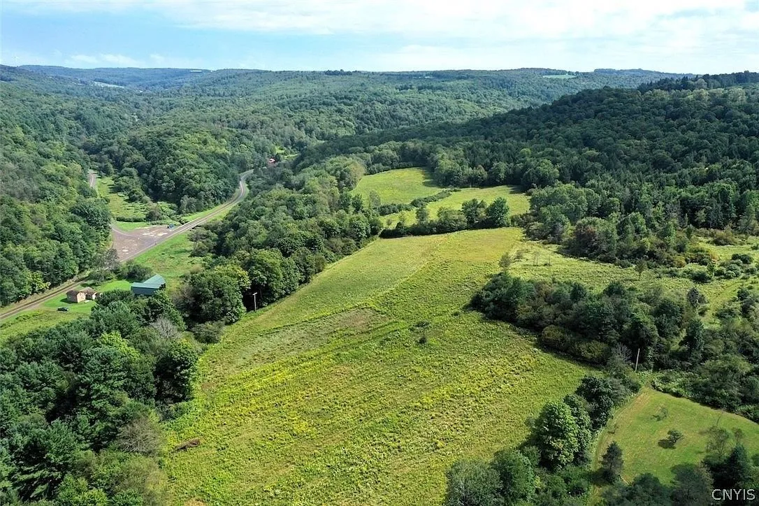 The fields and the wooded hills from the air with the buildings small at the left
