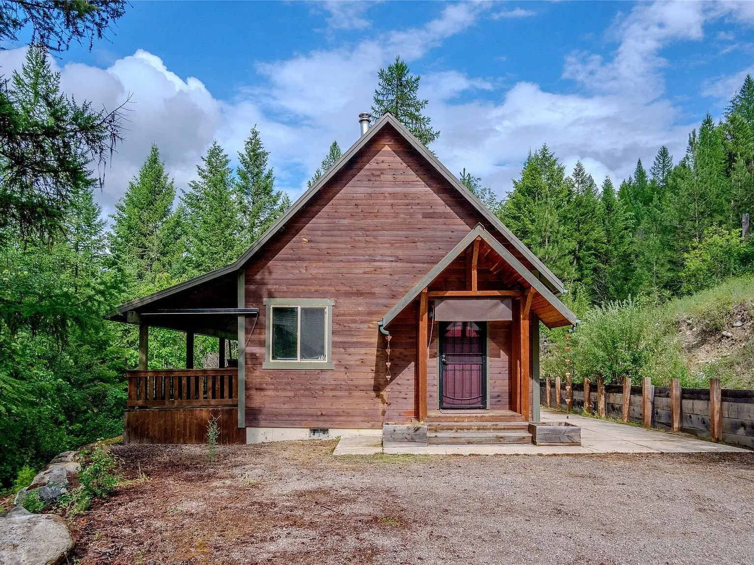 The front of the cabin among tall pines, covered porch and entry door visible