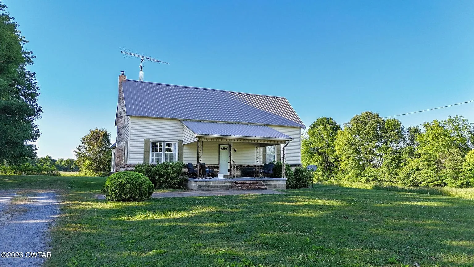 The farmhouse across the lawn with the porch and the drive to the right