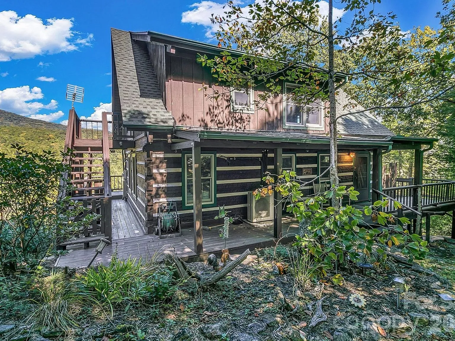 The log cabin among trees, with its covered porch and deck visible