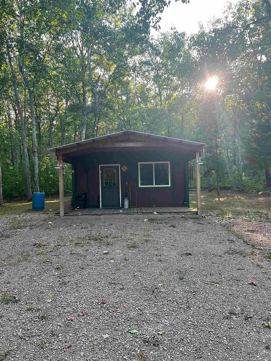 The cabin from the gravel yard with the sun through the trees