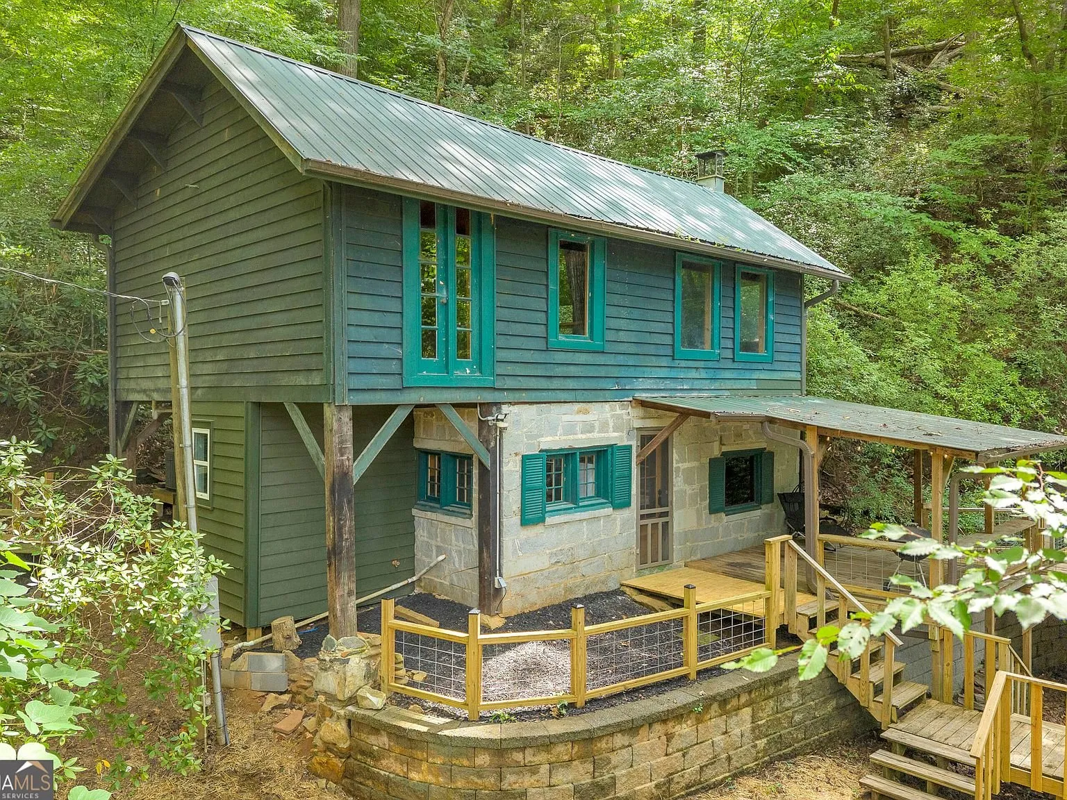 The cabin's exterior, stone first level and teal-trimmed wood siding above, seen from the yard