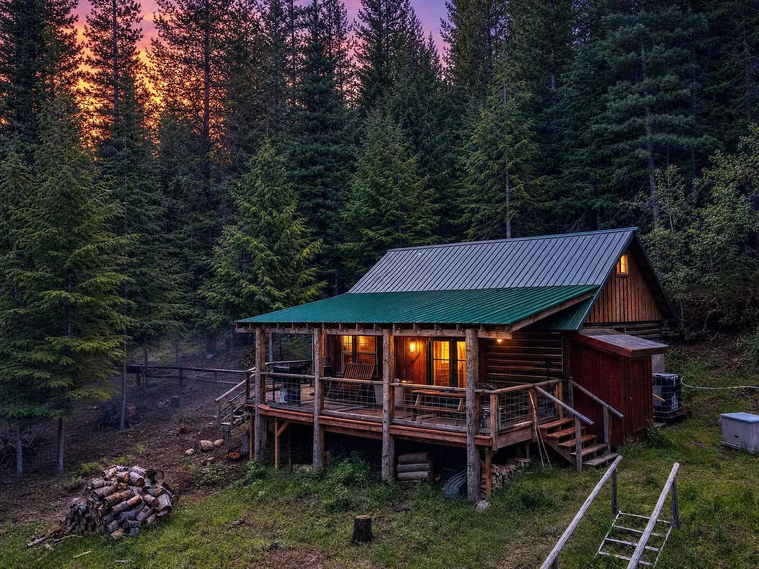 The cabin's red siding, covered porch and firewood stacked below, seen from the yard