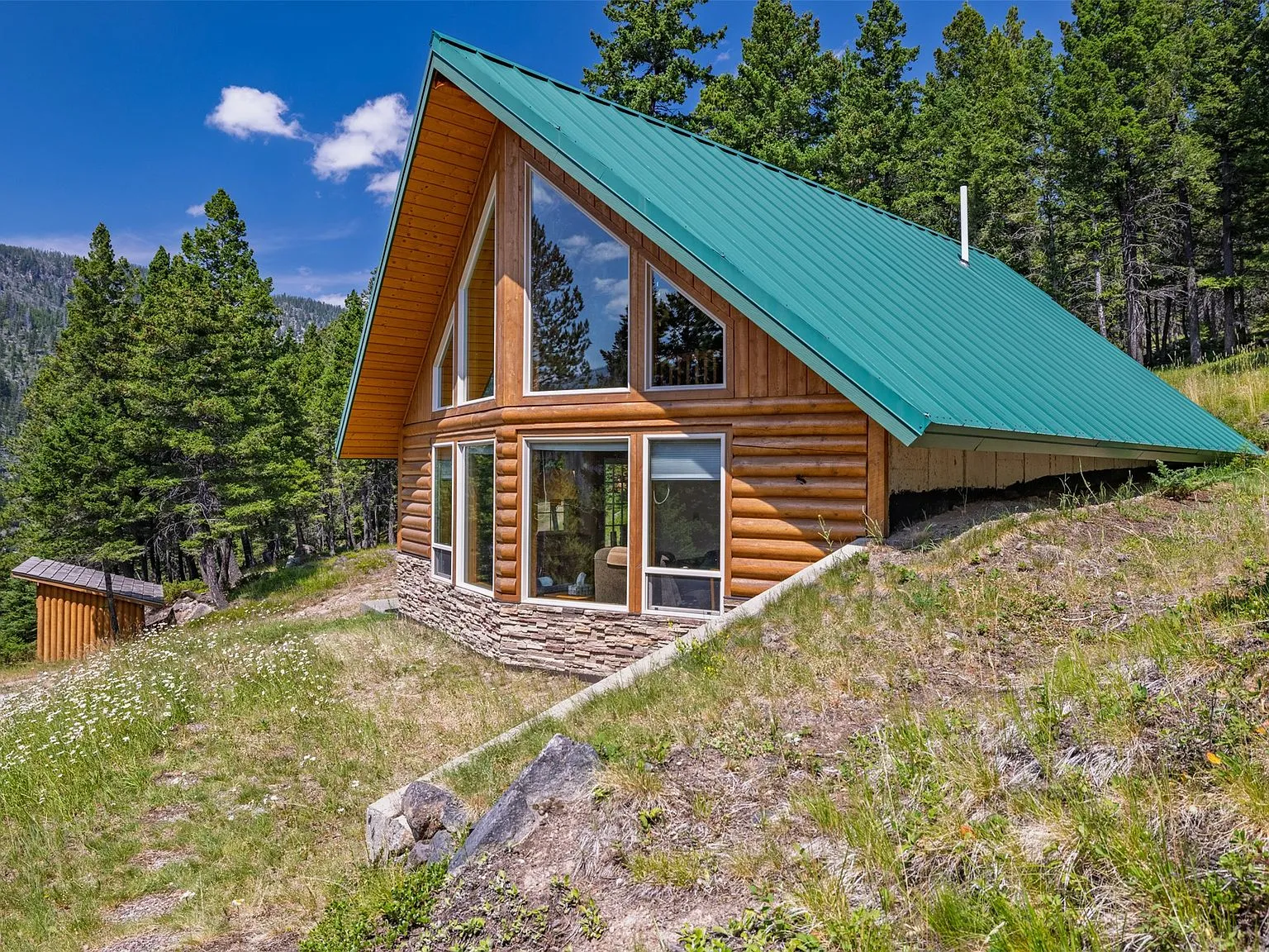 The A-frame cabin's front gable and floor-to-ceiling windows, seen from the yard