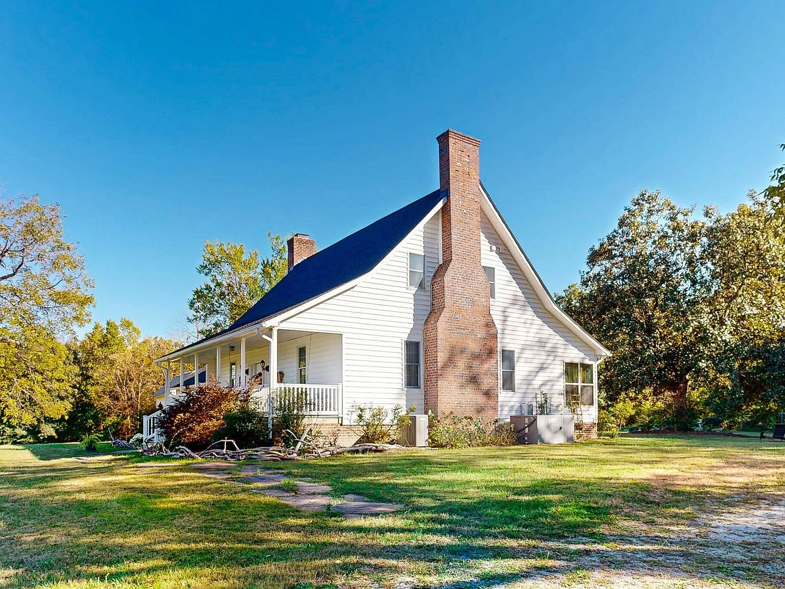 The farmhouse's front porch and brick chimney seen across the lawn
