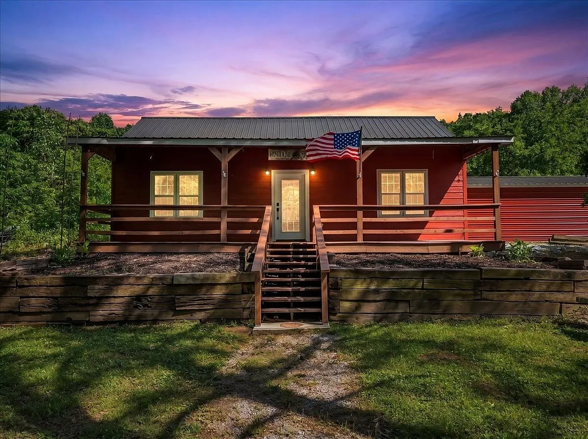 The same cabin at dusk, porch lights on and an American flag hanging by the door