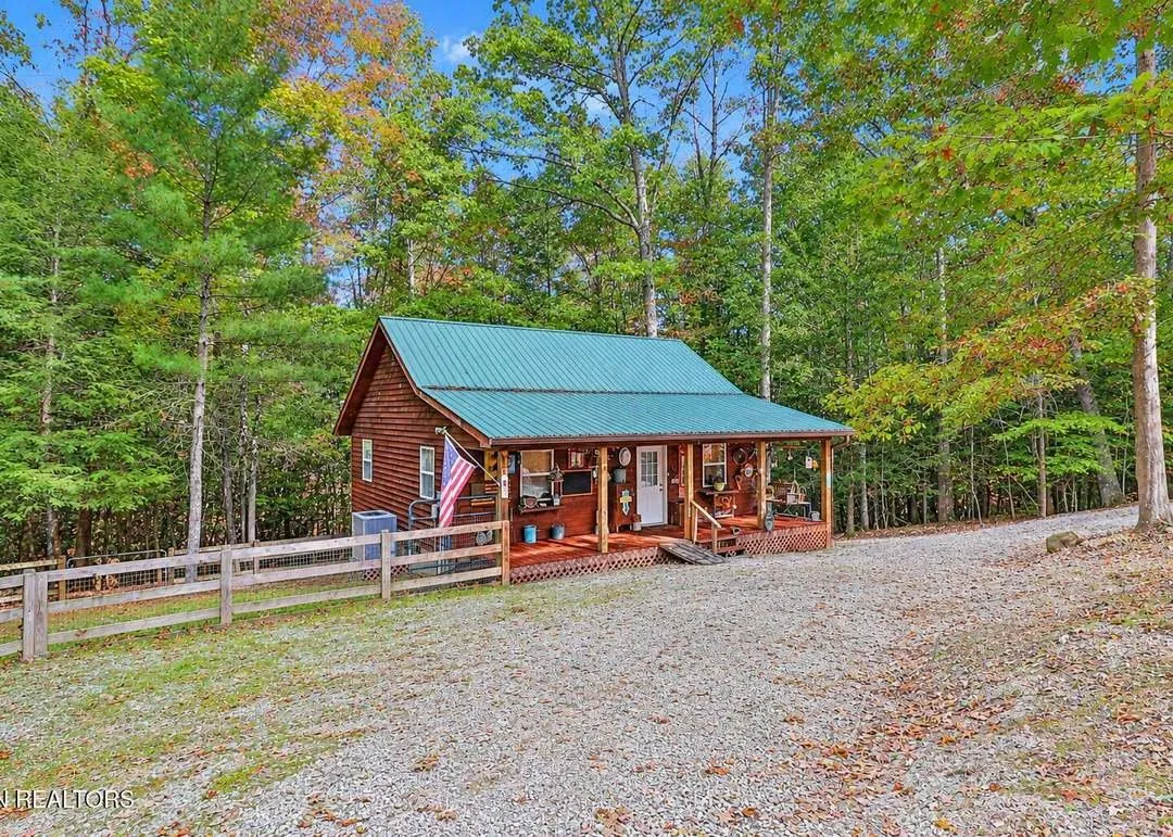 The cabin from a second angle, gravel driveway curving toward the covered entry