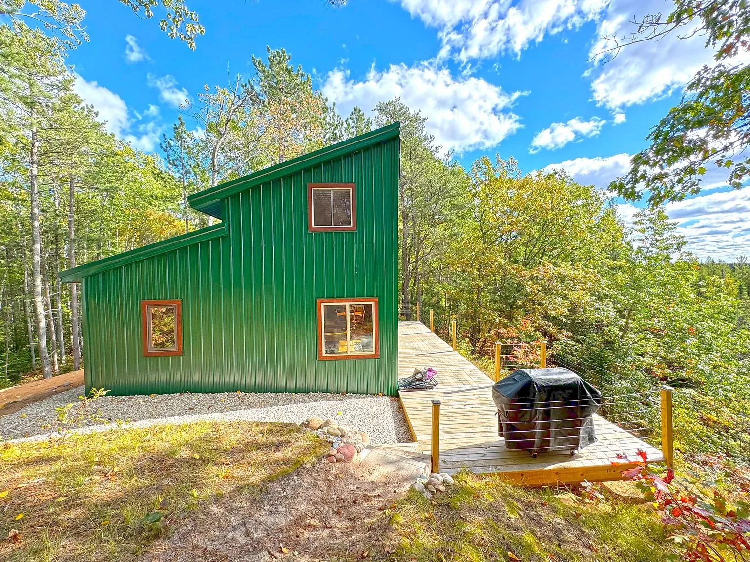 The green gable end of the cabin above the gravel pad, deck and water tank alongside