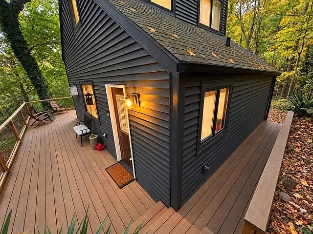 The cabin's steep gable roofline and dark vertical siding, seen among tall trees