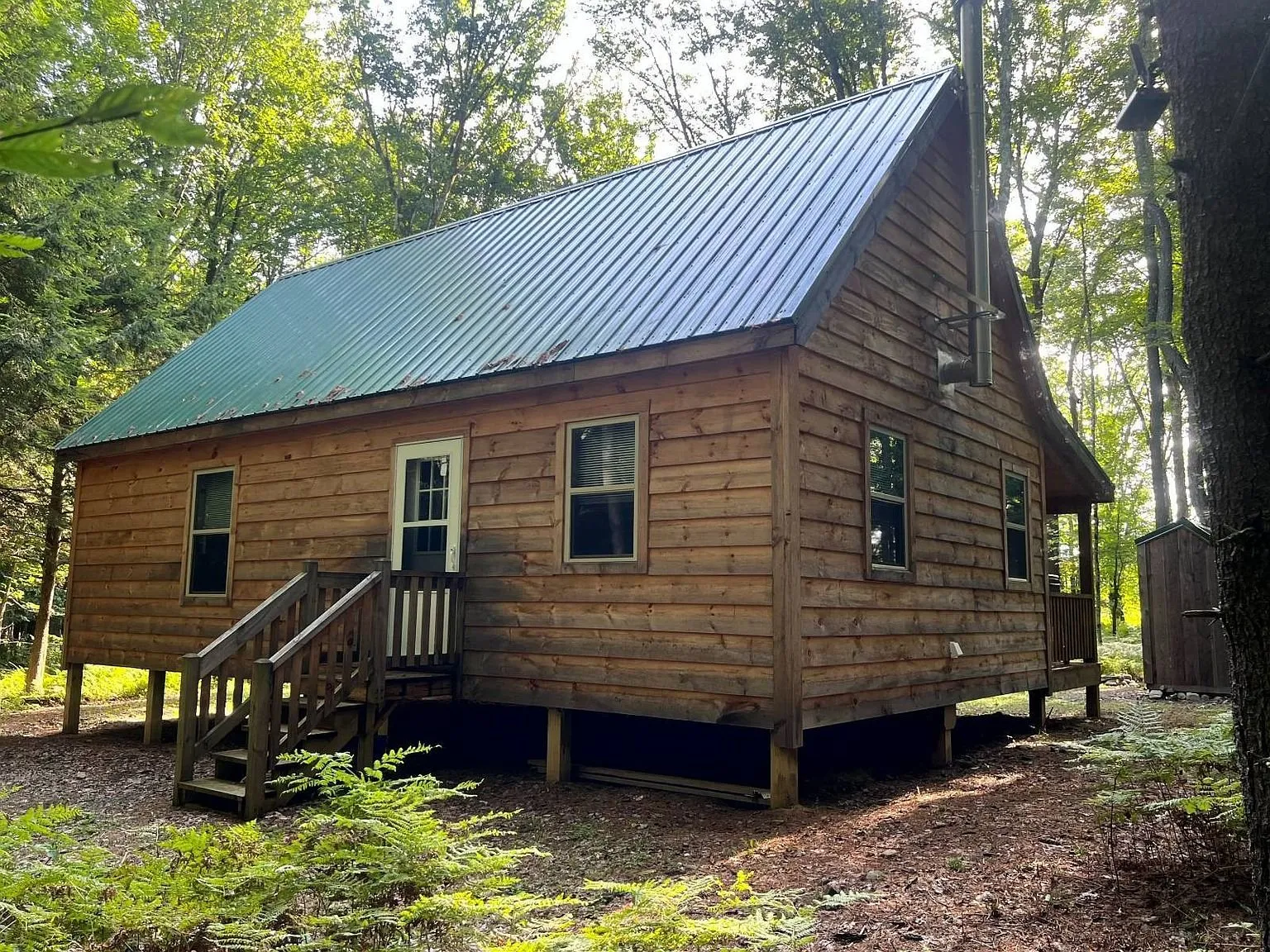 The side of the cabin with the porch steps and the woods behind