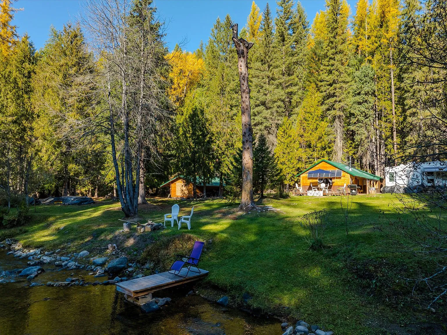 An aerial view of the cabin, creek and surrounding clearing framed by autumn larches