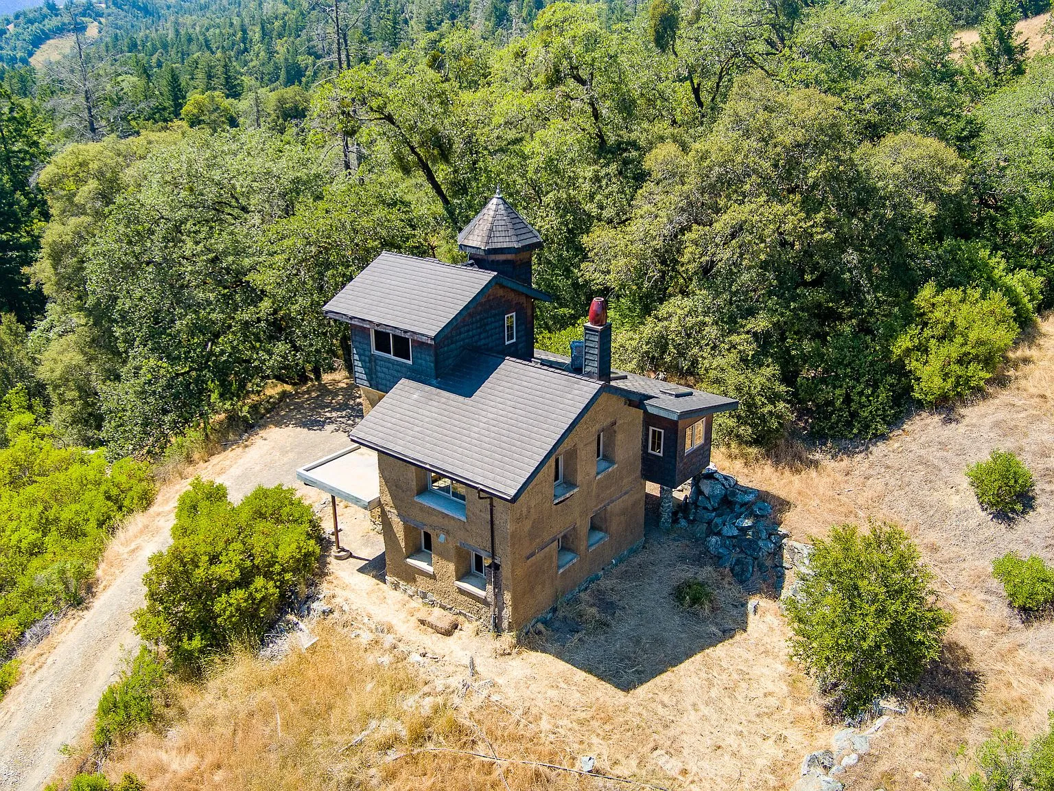A wide aerial view of the home perched above the surrounding meadows and forest