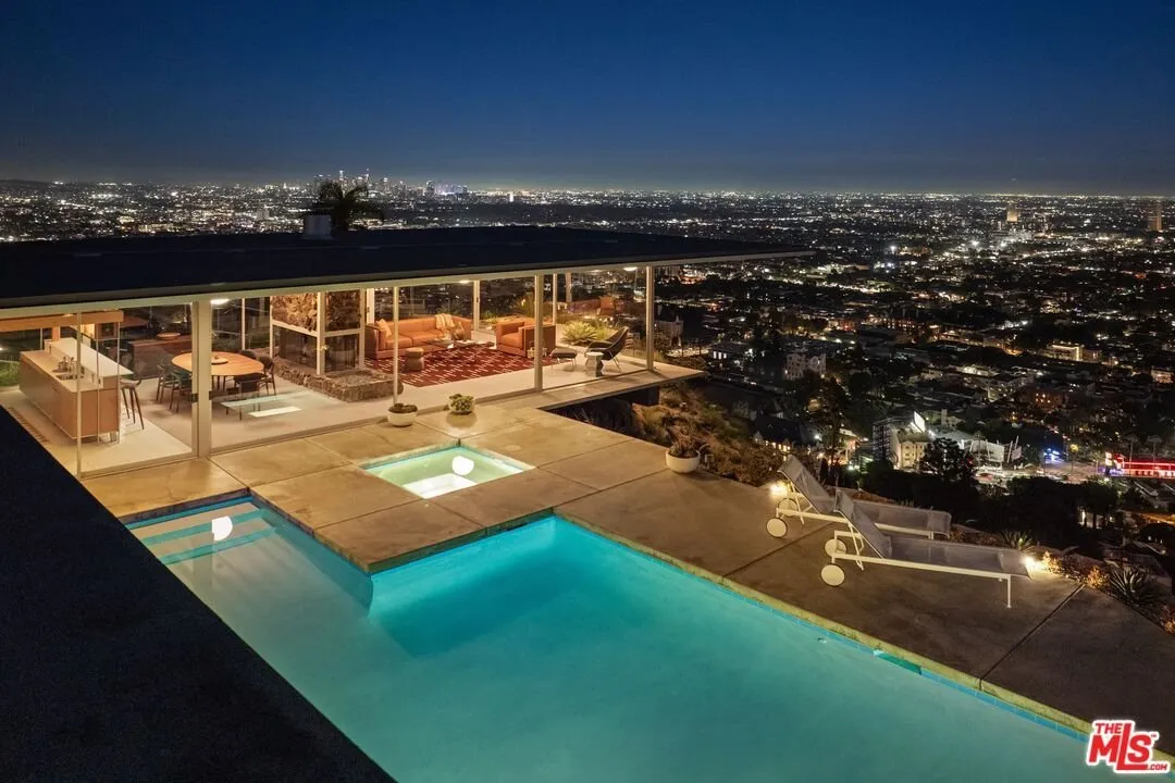 Aerial at dusk of the pool deck and the lit interior above the city grid