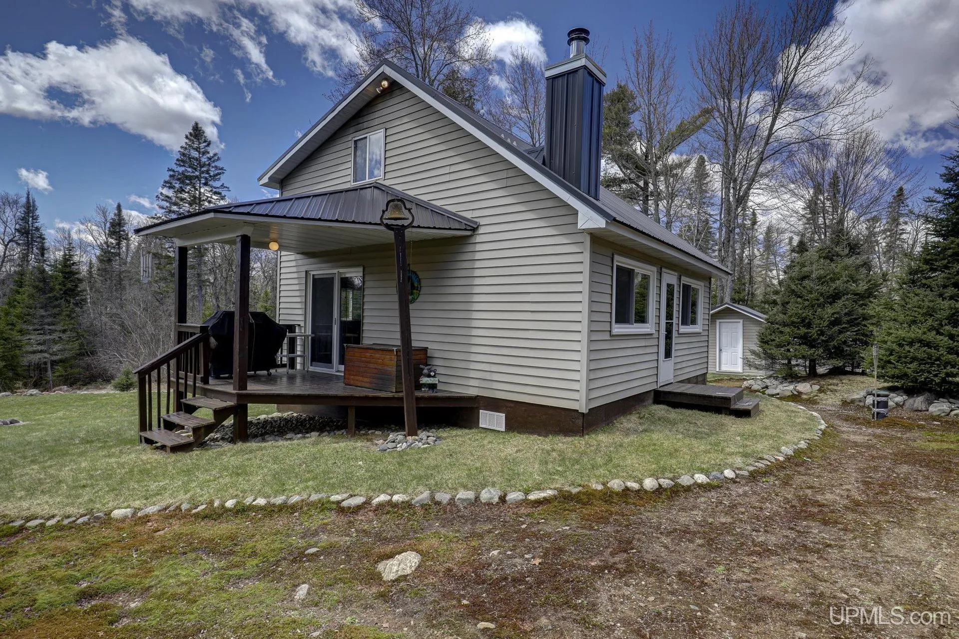 The side of the cabin with the deck, the stovepipe and a stone-lined bed along the wall