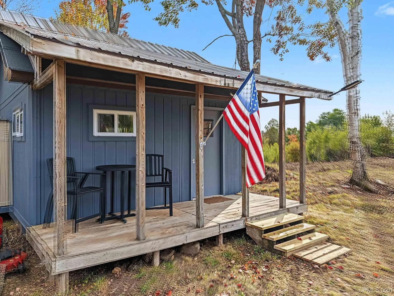 The front porch with chairs and a flag, steps down to the yard