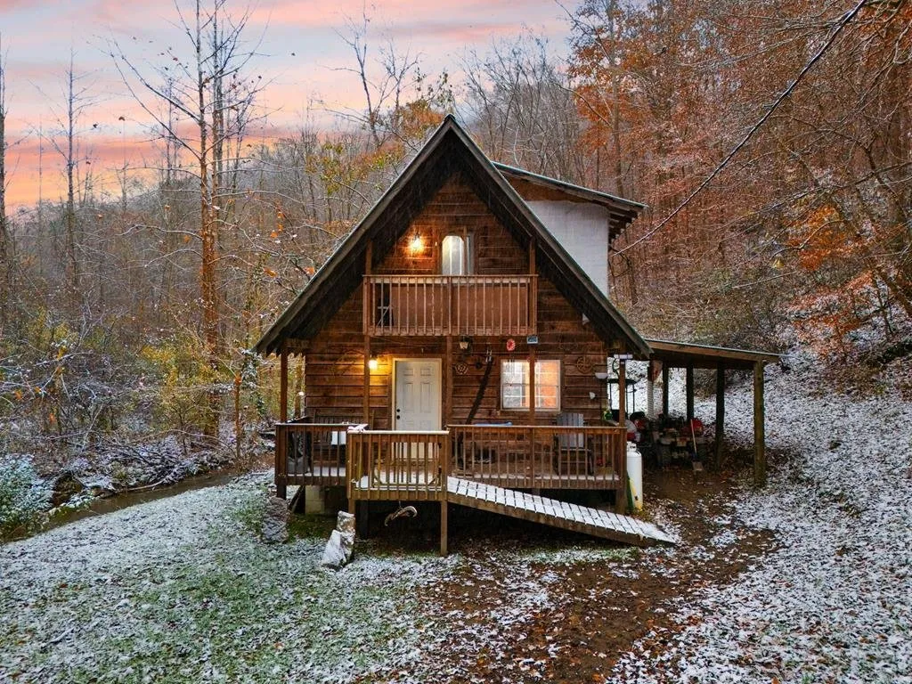 The cabin at dusk with the porch and balcony lights on, snow on the ground