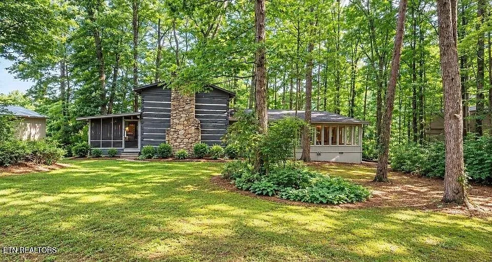 The grey-sided house and screened porch across the mown lawn