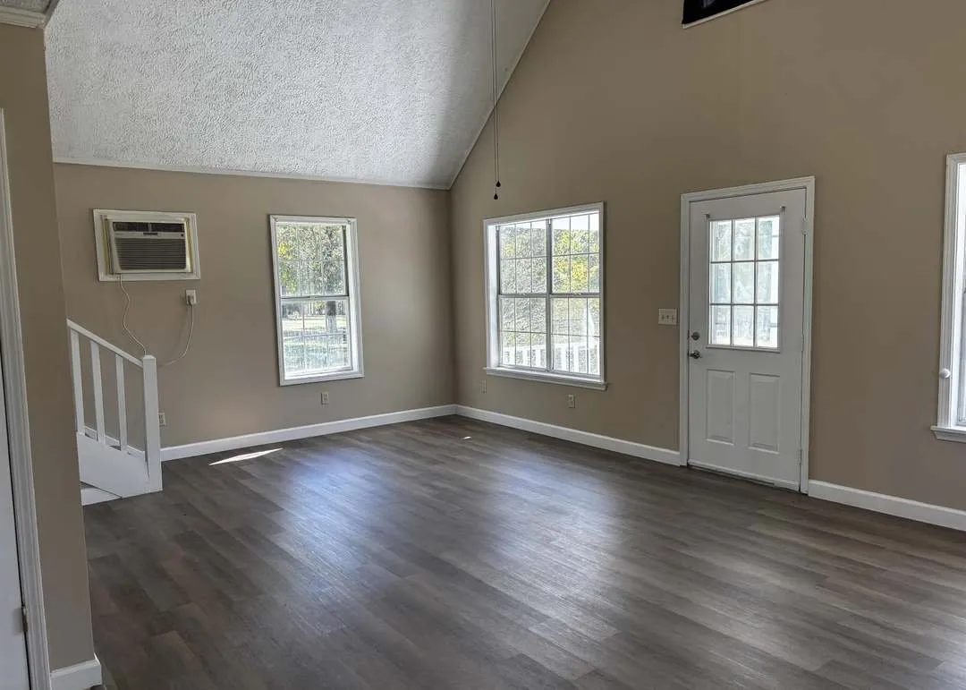 The vaulted living room with wood-look flooring and tall windows