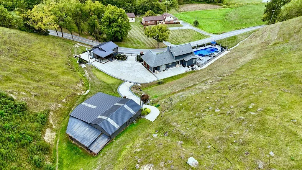 Aerial looking down on the house and the blue pool from above the ridge