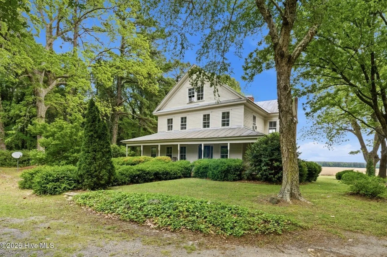 Side of the house with the metal roof and wrap-around porch, open field beyond