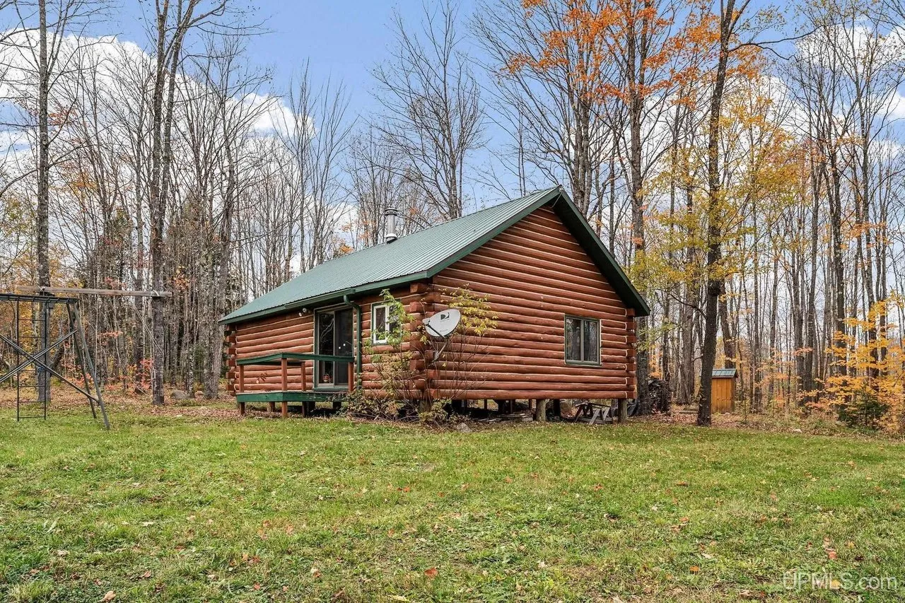The cabin across the mown clearing, hardwoods rising behind it