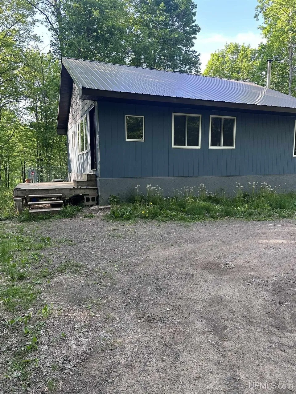 The cabin from the gravel yard with its metal roof and the side steps