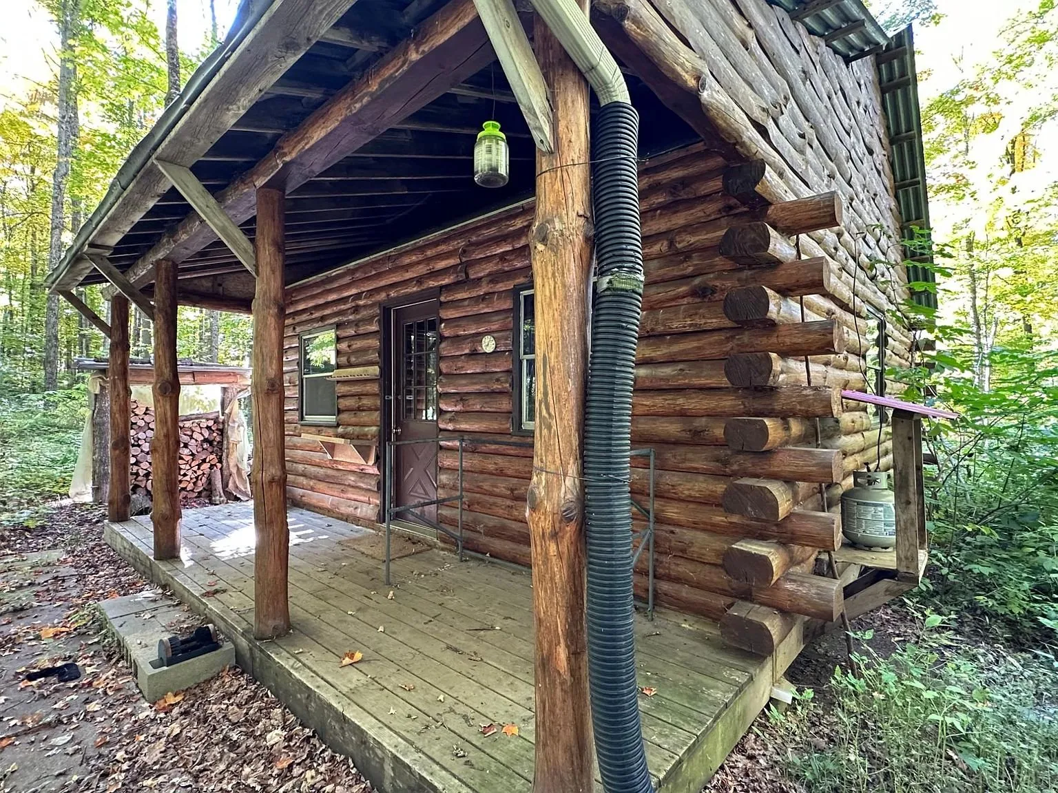 The covered porch with peeled log posts and split firewood stacked behind