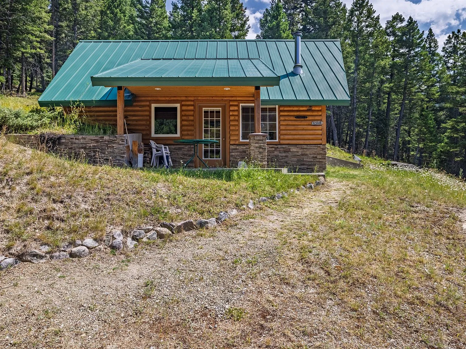 The cabin standing in a clearing at the end of the gravel driveway