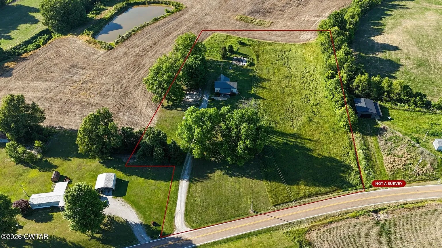 Aerial with the parcel outlined in red, the house among the trees, two outbuildings, the road and the fields around it