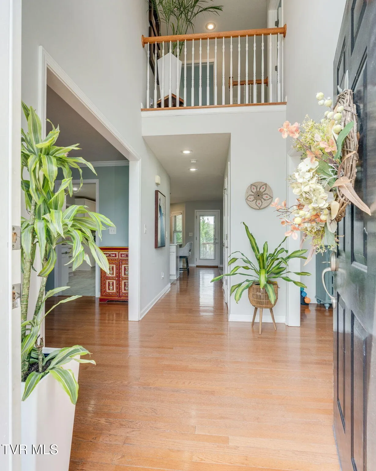 The entrance foyer with hardwood floors and the open stair rail on the landing above