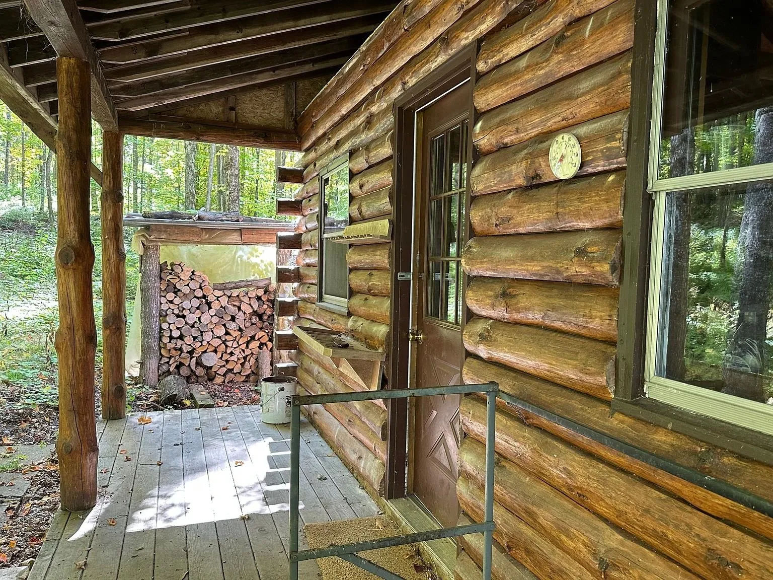 Along the porch deck, log wall and window with the woodpile beyond