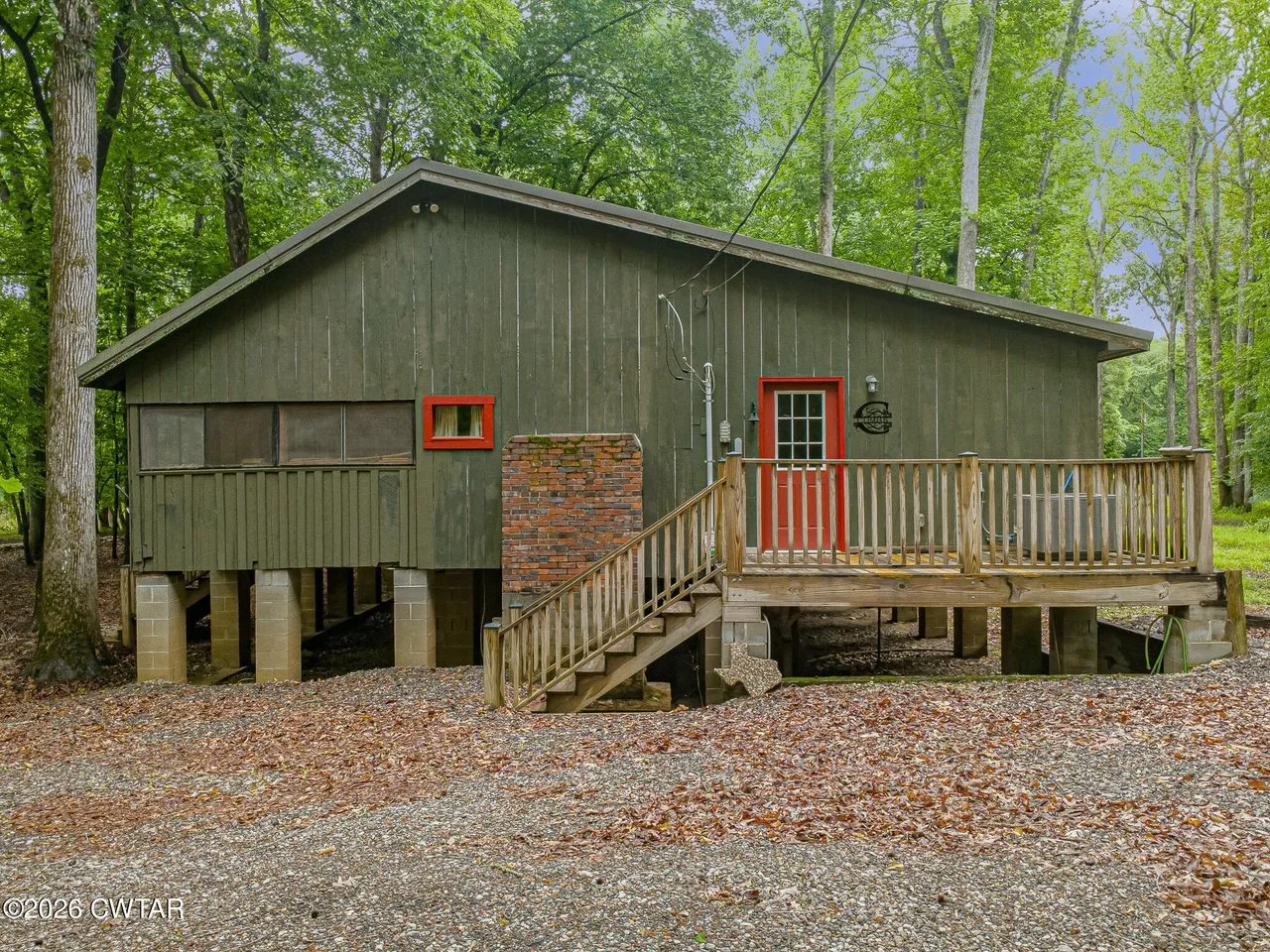 The front of the cabin, red door and window trim against the green siding