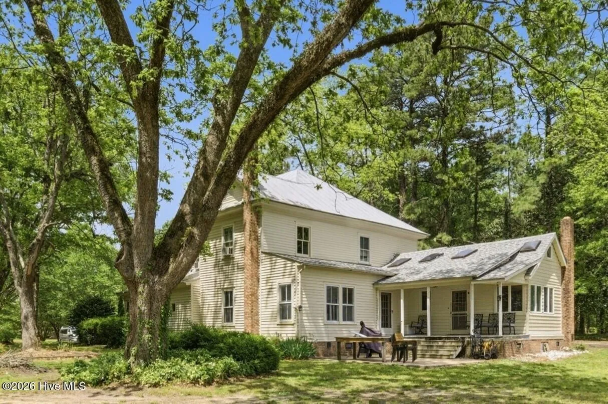 Rear of the house under a large hardwood, two brick chimneys and the back porch
