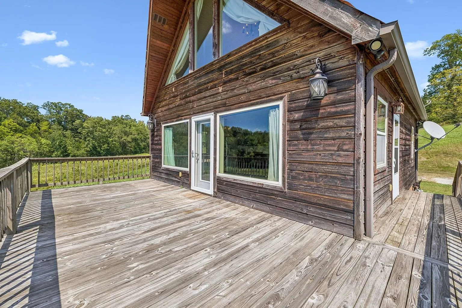 The deck along the side of the house with the sliding door and the field beyond