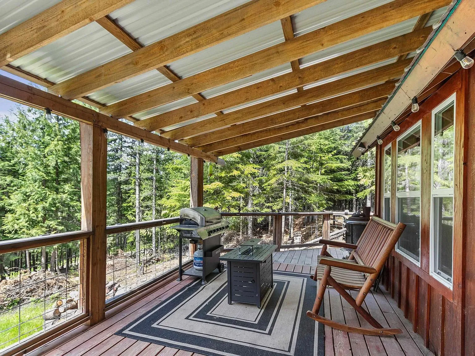 The covered deck with a metal roof, outdoor rug and Adirondack chair overlooking the trees