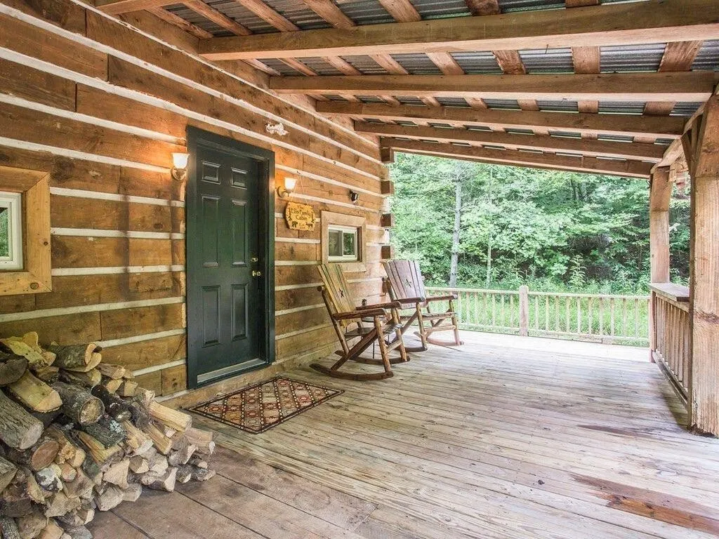 The covered porch with rocking chairs, a stacked woodpile, and the front door