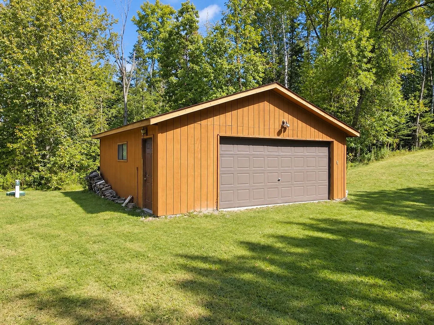 The detached garage with its overhead door at the edge of the woods