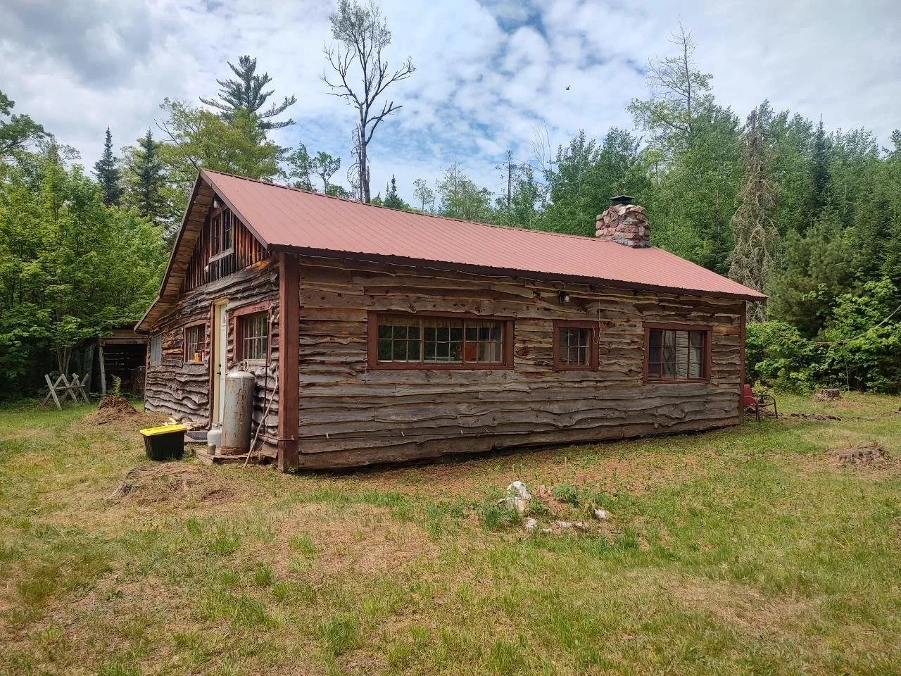 The log camp and its stone chimney from the corner of the clearing