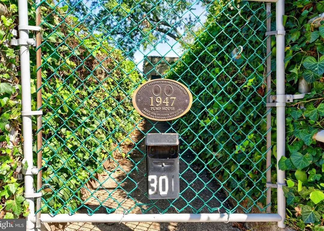 A chain-link gate with a plaque reading 1947 Pump House