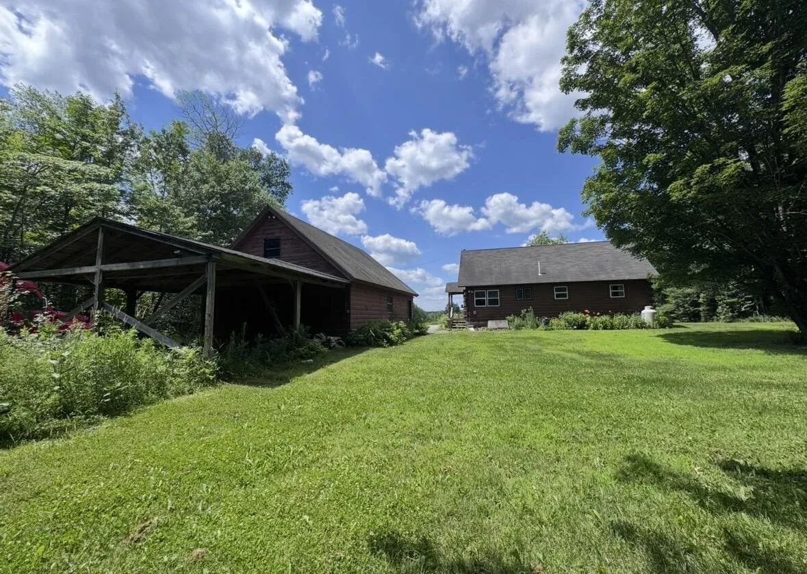 The lean-to, the garage and the cabin from the back lawn under a blue sky