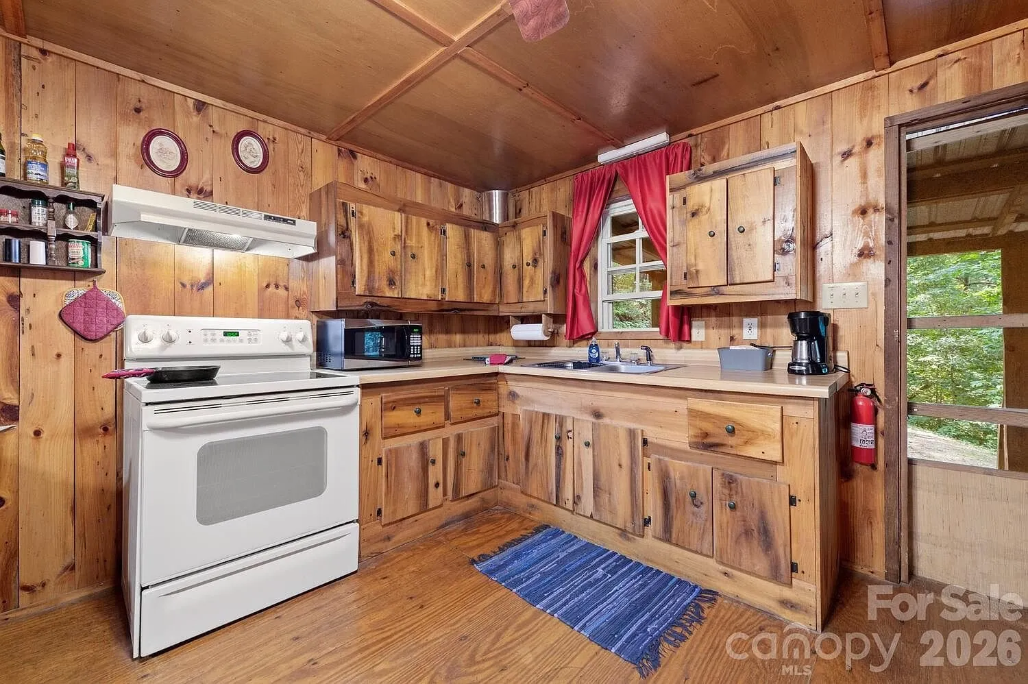 The kitchen with the electric range, the pine cabinets and the red curtains
