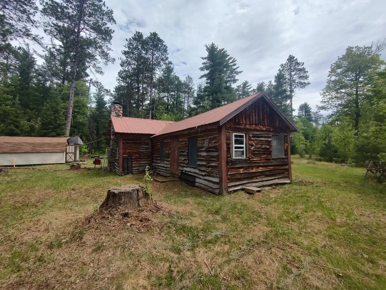 The far end of the camp with a stump in the foreground and an outbuilding beyond