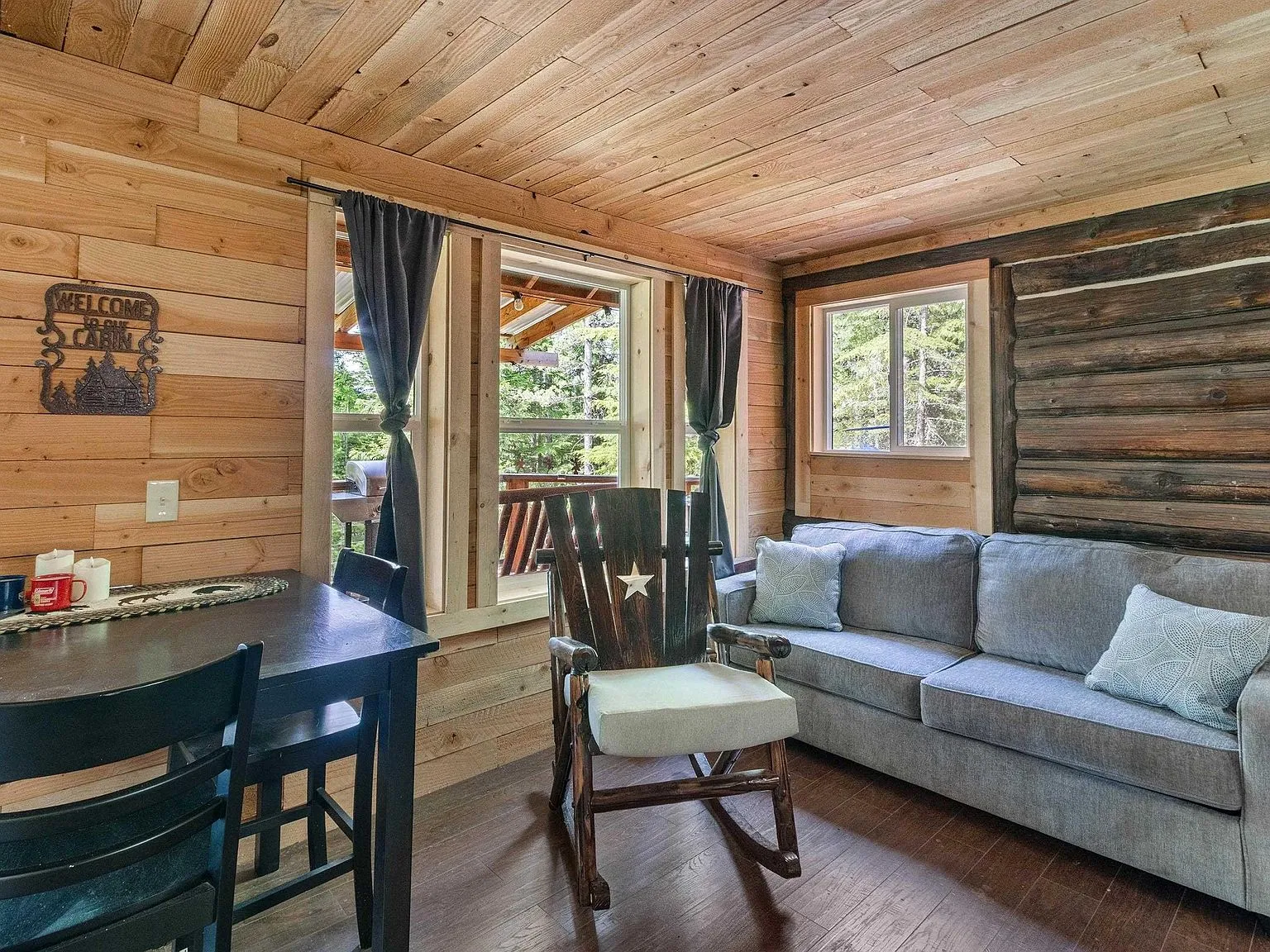 The living room with a rocking chair, sofa and windows looking out at the forest
