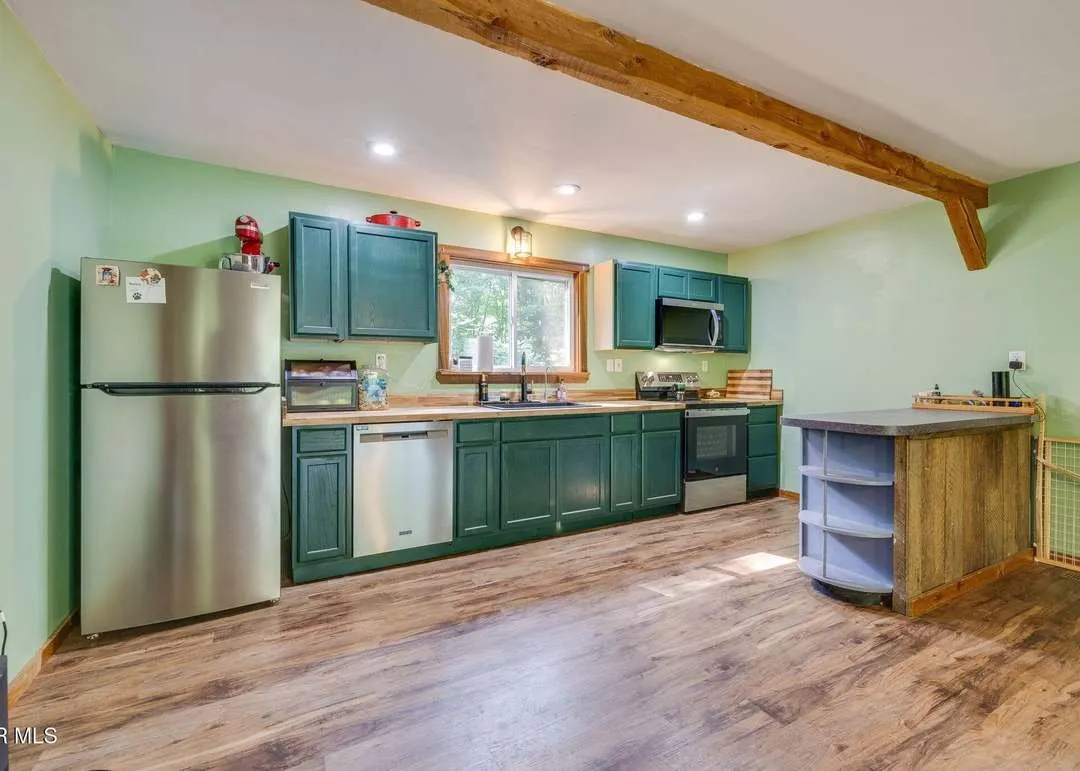 The kitchen with green cabinetry opening into the living space