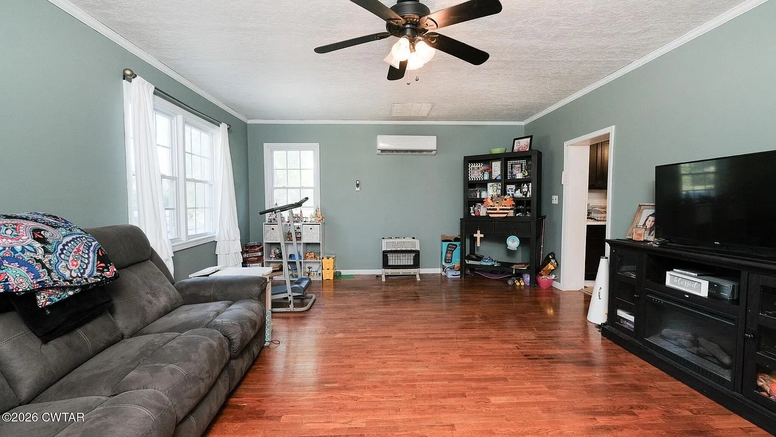 The living room with hardwood floors, a sectional and a mini-split head above the windows