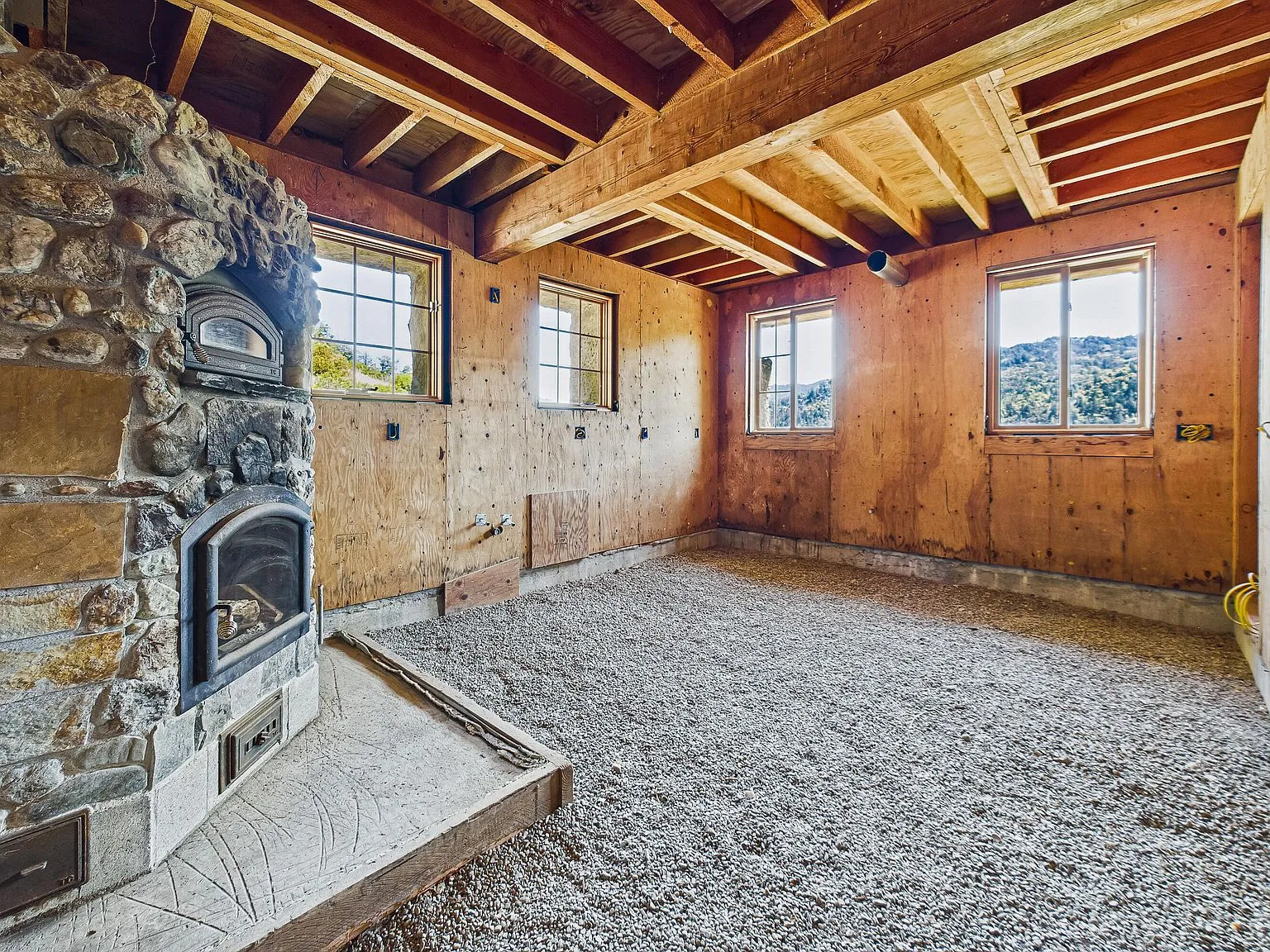 The unfinished great room with exposed Douglas fir framing and a stone masonry heater