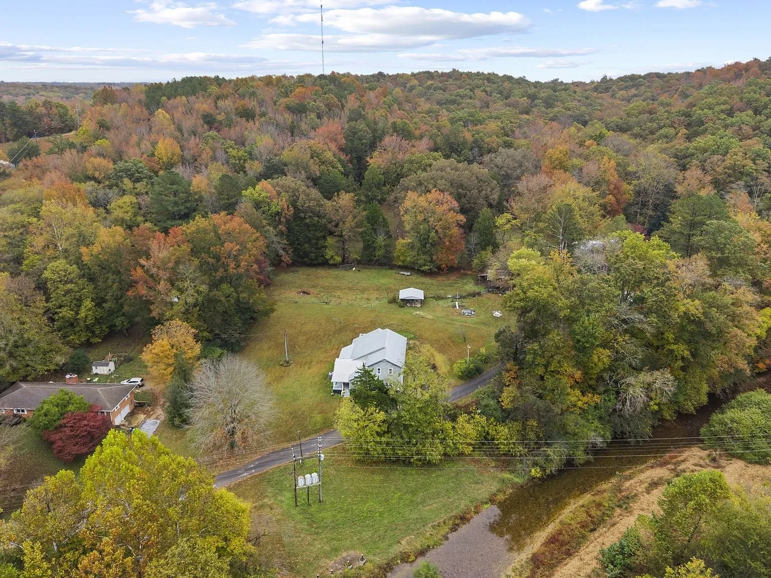 Aerial from the other side: the house, the outbuildings, and the creek line along the road