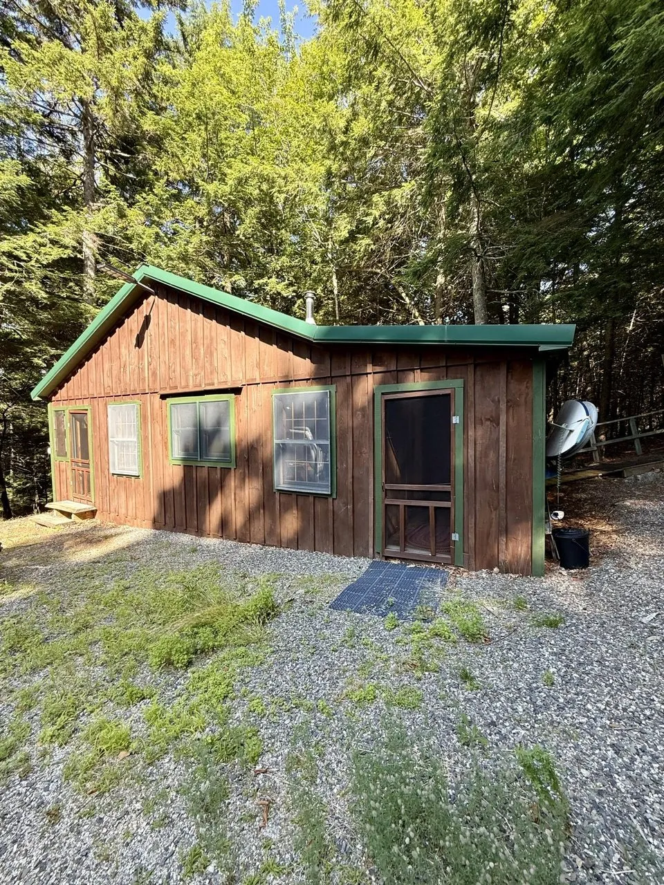 The camp from the front with the screen door, a solar panel on the ground and the satellite dish