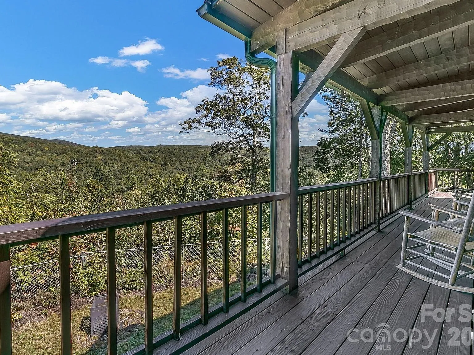 A covered deck with a rocking chair and a mountain view beyond the railing