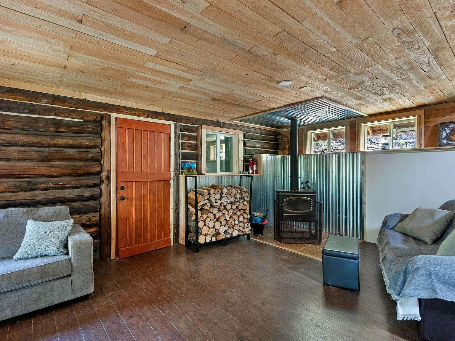 The living area's wood stove with a stacked firewood nook built into the corrugated metal wall